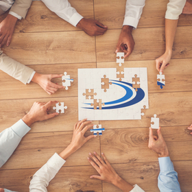 Des personnes assemblent un puzzle du logo d'UniDistance Suisse, vue plongeante
