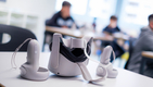 Im Vordergrund eine VR-Brille mit den Handsticks liegen auf dem Tisch, im Hintergrund sind Kinder erkennbar.